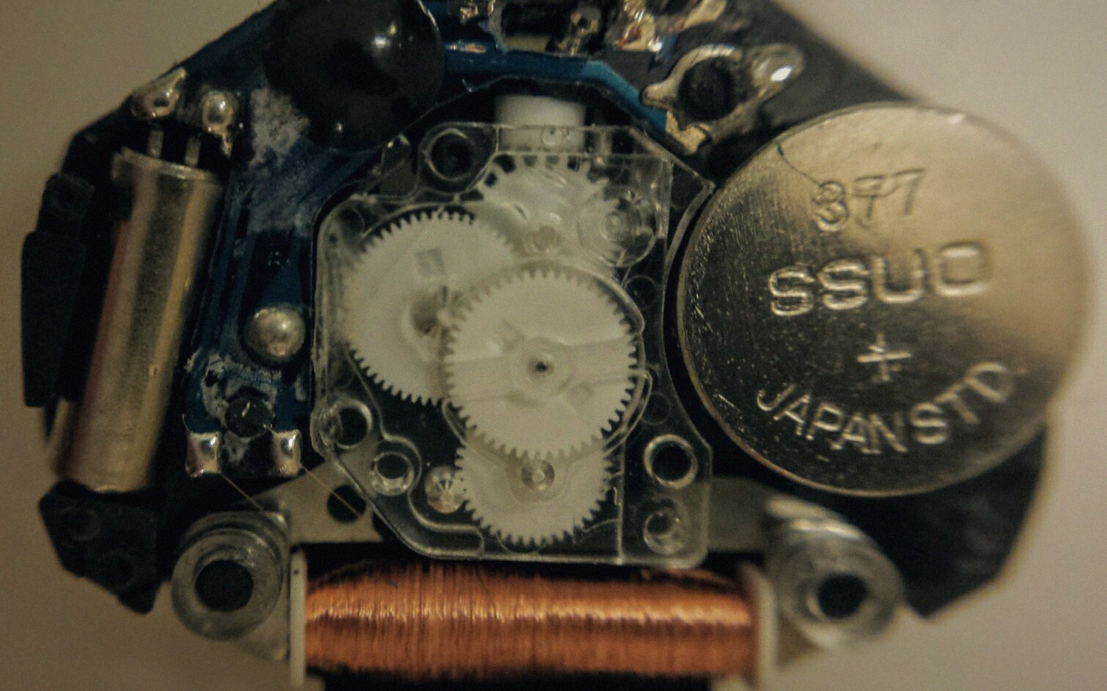 A tiny quartz tuning-fork resonator out of its can, on a white surface beside a sewing needle for scale, macro