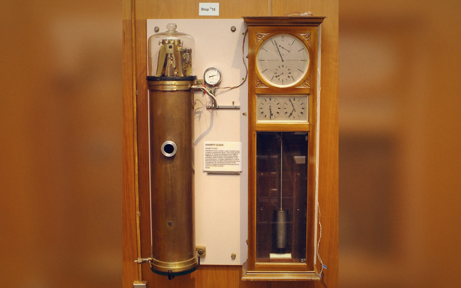 A tall cylindrical vacuum tank containing a pendulum, mounted on a wall in an observatory basement, cold even light